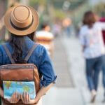 Mulher de costas, com mochila, diante de um mapa, representando o tema empréstimo para viajar.