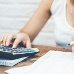 Mulher usando calculadora com papéis na mesa, ilustrando o tema Portabilidade de Crédito.