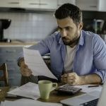 Homem sério olhando para um papel, representando o tema 'gestão financeira pessoal'