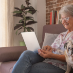 Idosa sentada sorrindo enquanto mexe no computador, demonstrando interesse em empréstimo consignado.