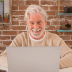 Idoso sentado no computador sorrindo, interessado em informações sobre empréstimo consignado INSS.