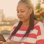 Idosa sorrindo enquanto mexe no celular, buscando informações sobre empréstimo para aposentado.