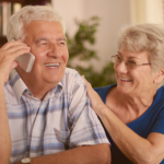 Casal sorrindo, com o idoso conversando ao celular sobre empréstimo consignado.