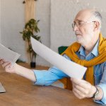 Homem adulto comparando folhas de aposentadoria