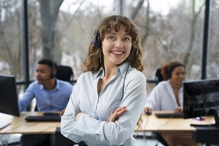 Mulher sorrindo com colegas ao fundo trabalhando no computador, representando o 13° salário em Alagoas.