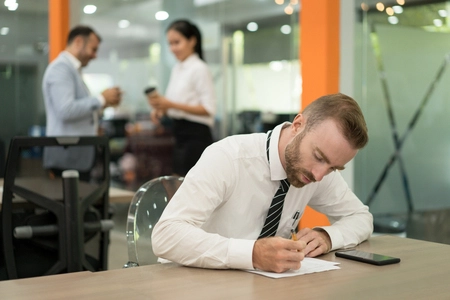 Homem sentado no trabalho, escrevendo em um papel, representando o tema FGTS e PIS são a mesma coisa.